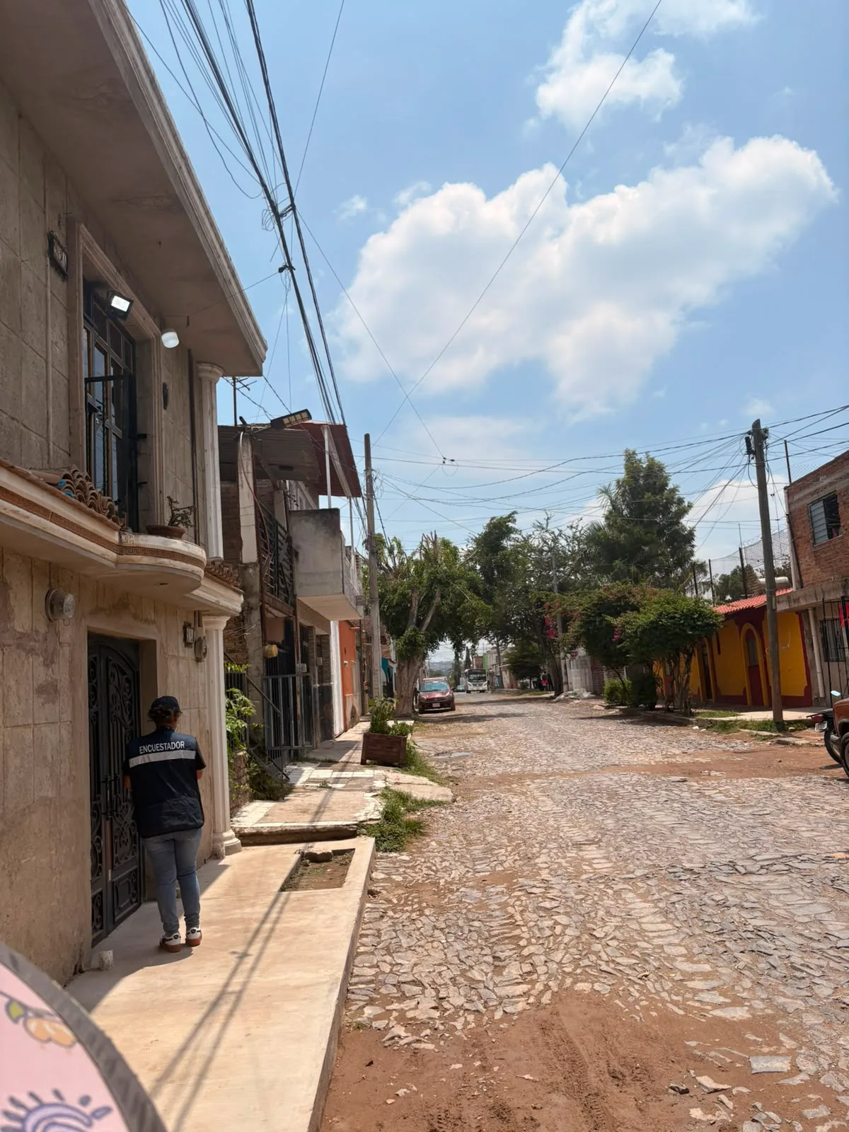 Encuestadora de CENESSOD tocando en una vivienda de una calle empedrada.